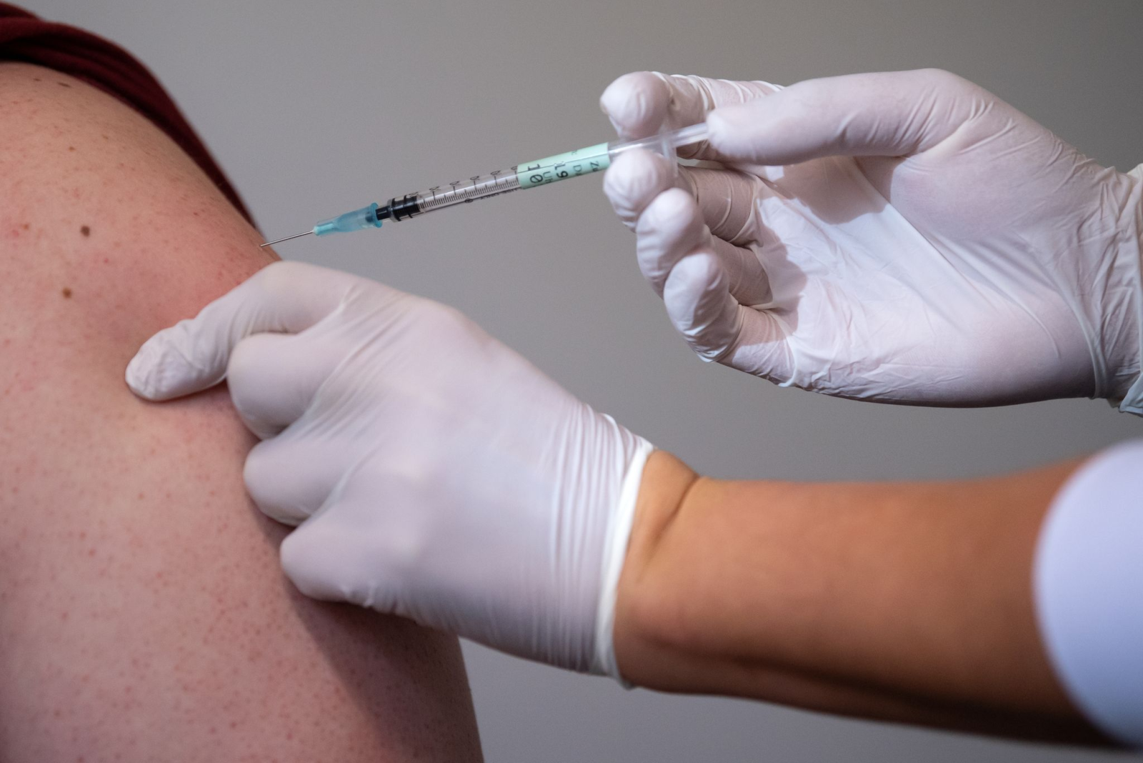 Eine Mitarbeiterin eines Impfzentrums impft einen Mann.