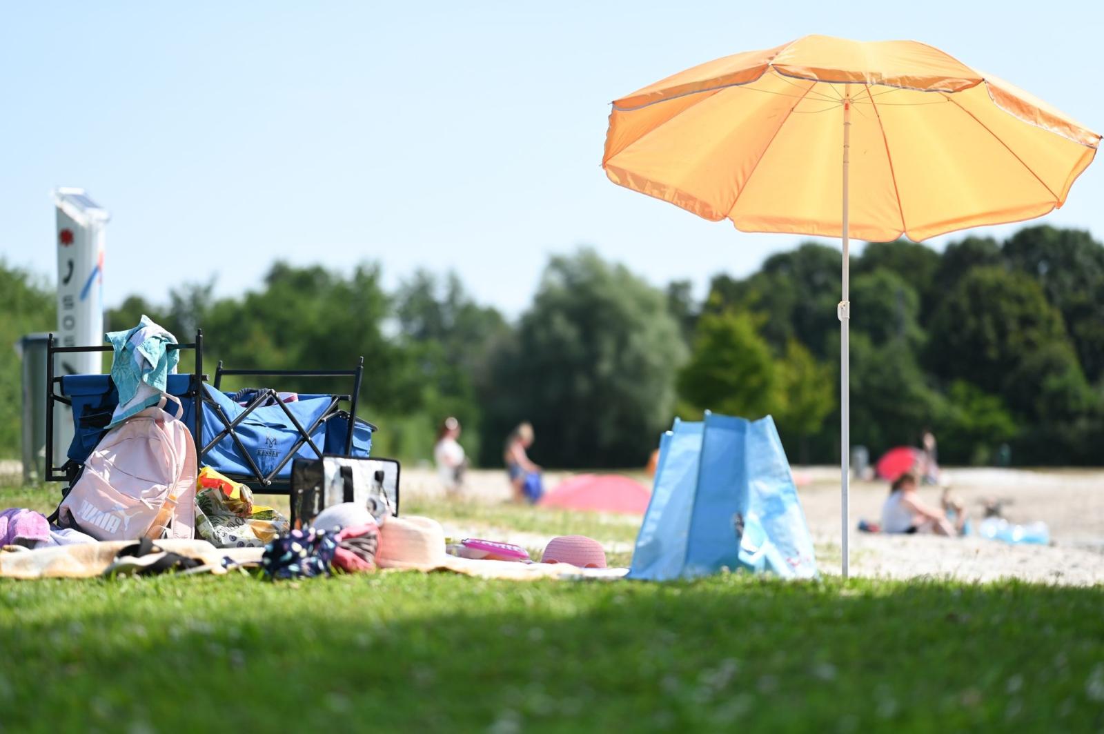 Eine Picknickdecke mit Sonnenschirm sind an einem Badesee zu sehen.