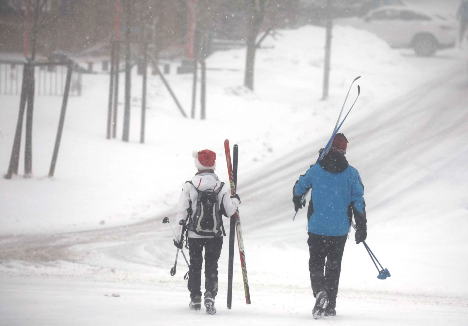 Wintersportler gehen mit ihren Skiern im Schneetreiben einen Weg entlang.
