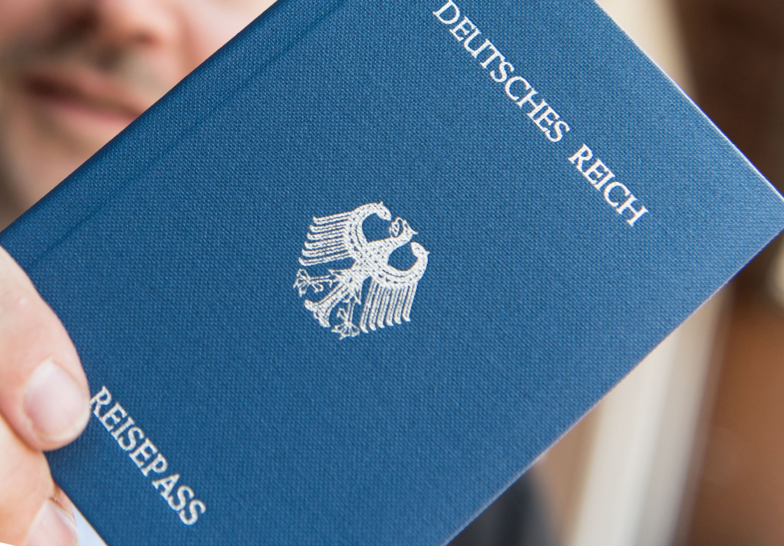Ein Mann hält ein Heftchen mit dem Aufdruck «Deutsches Reich Reisepass» in der Hand.