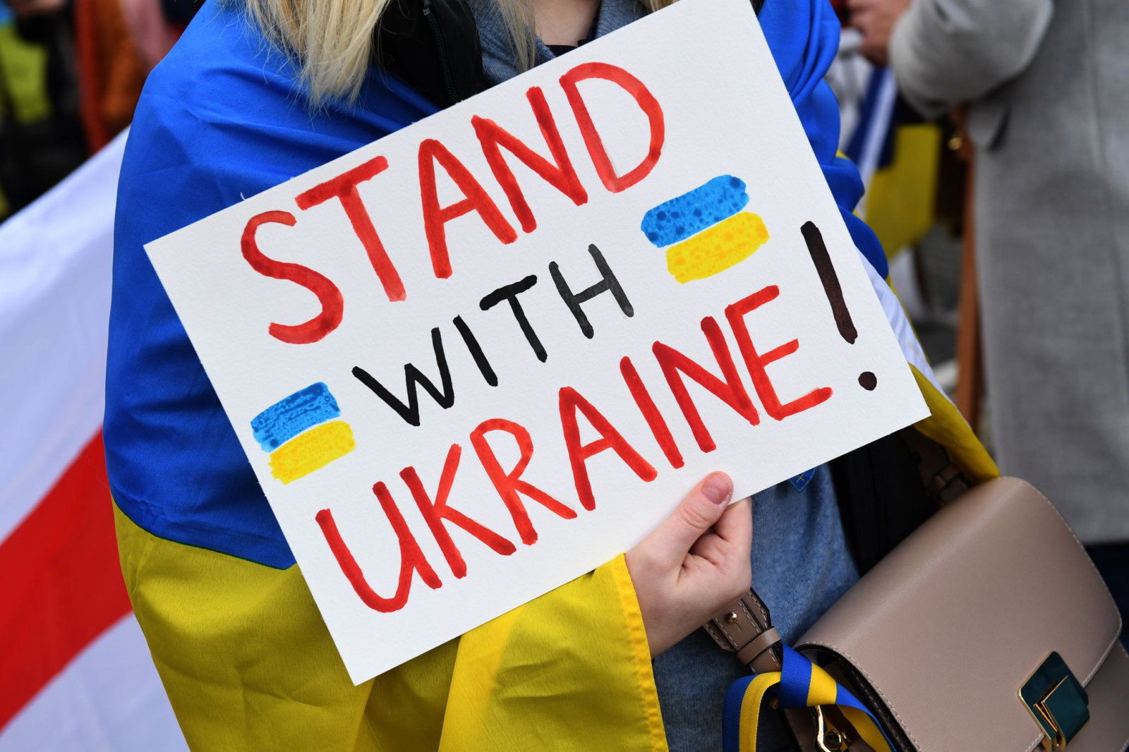 Eine Demonstrantin steht mit einem Plakat "Stand with Ukraine! " steht bei einer Demo für die Ukraine.