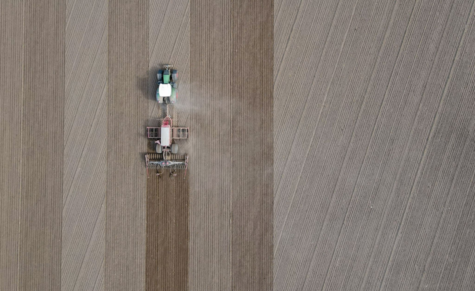 Ein Landwirt fährt mit seinem Traktor über ein Feld und bringt Saatgut in den Boden aus.