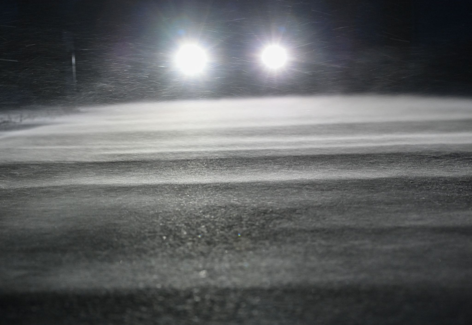 Die Scheinwerfer eines Autos scheinen über eine verschneite Straße.