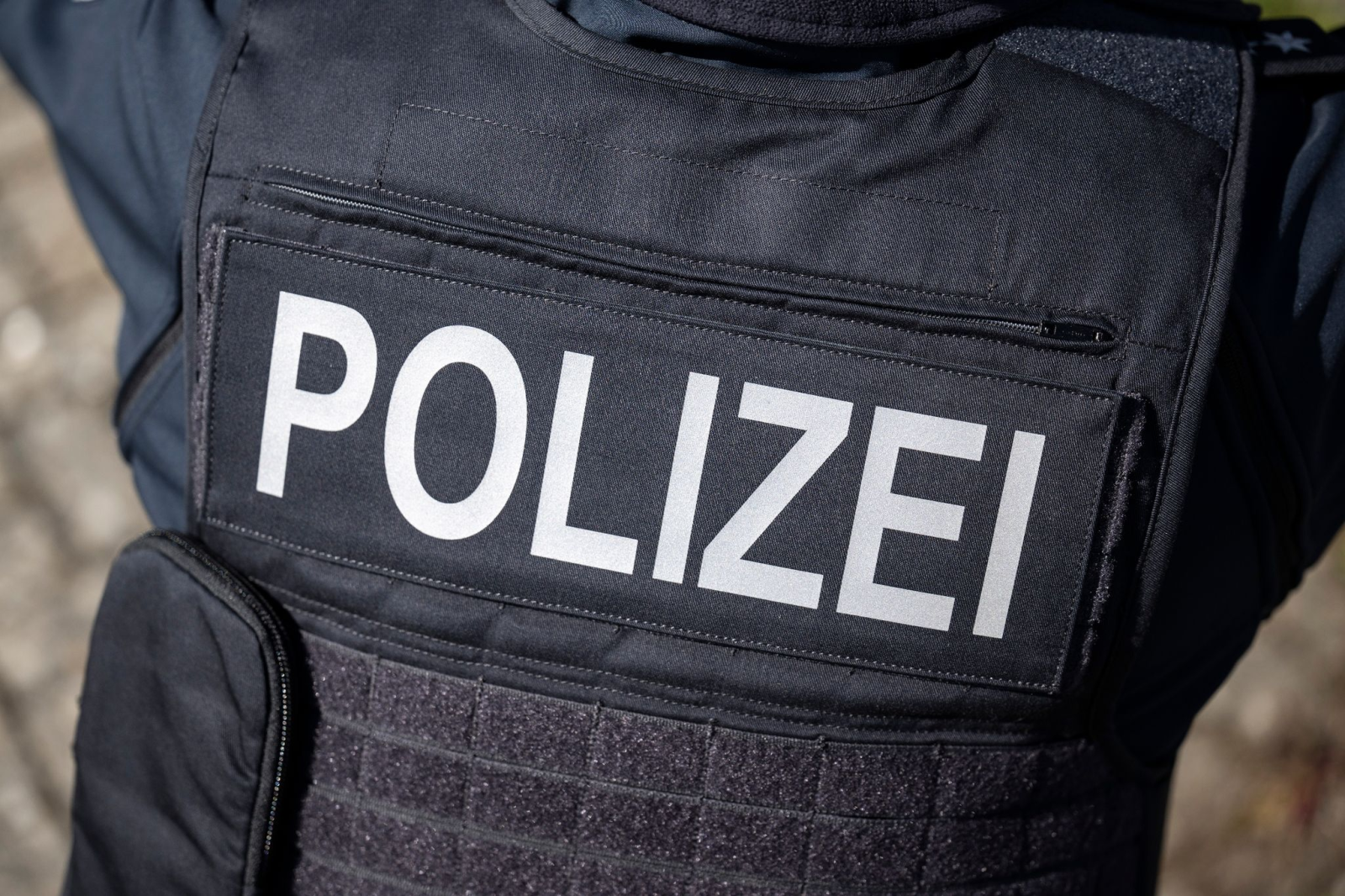 Ein Polizist trägt eine Schutzweste mit der Aufschrift «Polizei»., © Hannes P Albert/dpa/Symbolbild