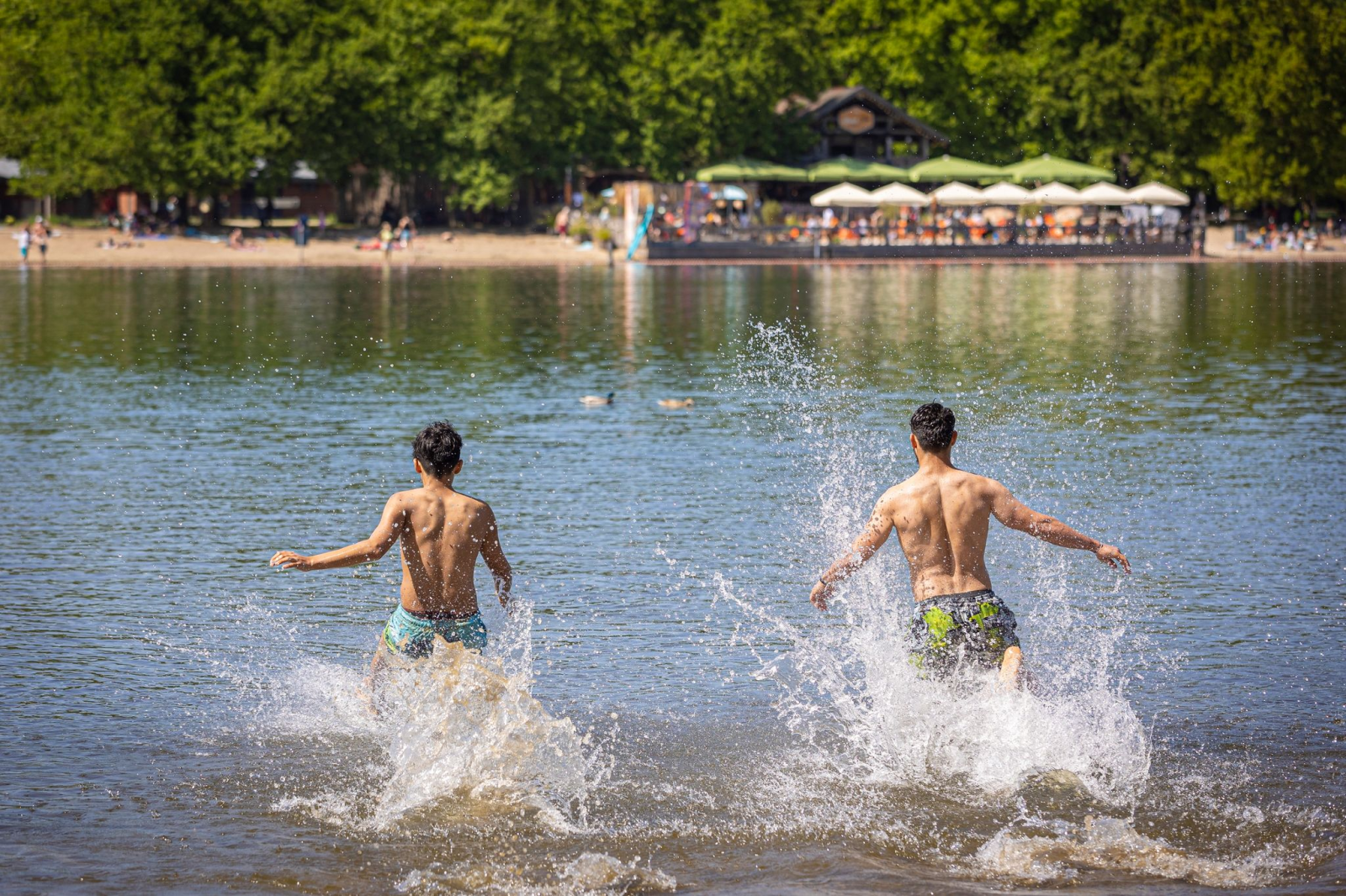 Zwei junge Männer rennen bei sonnigem Wetter in das Wasser.
