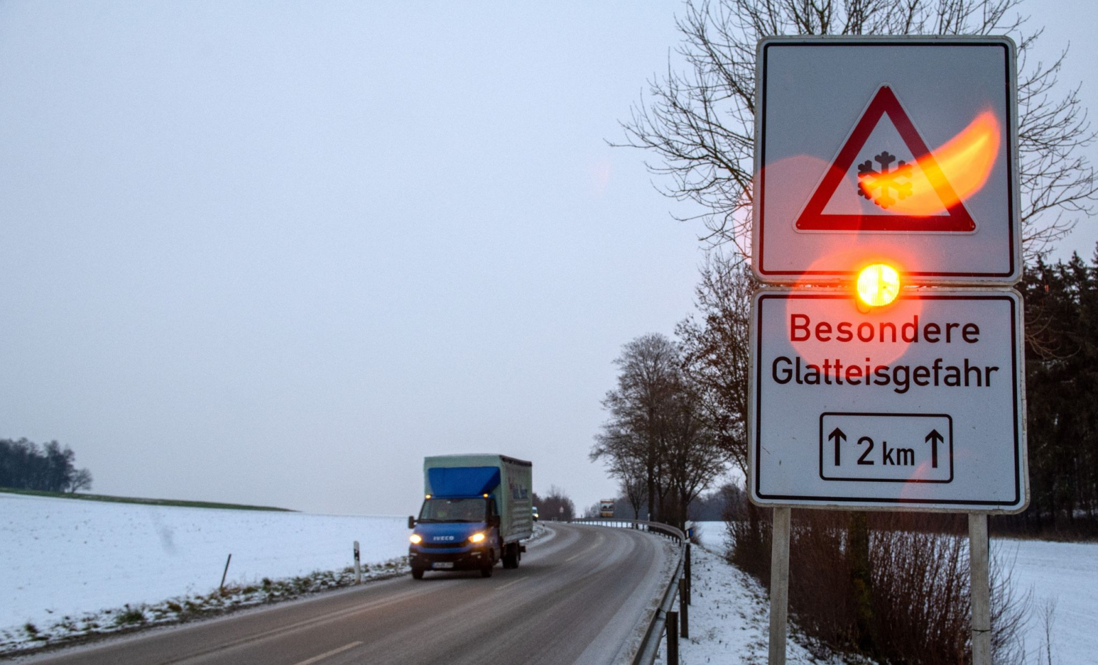 Ein Straßenschild warnt mit einer Blinkleuchte vor Glatteis., © Stefan Puchner/dpa/Symbolbild