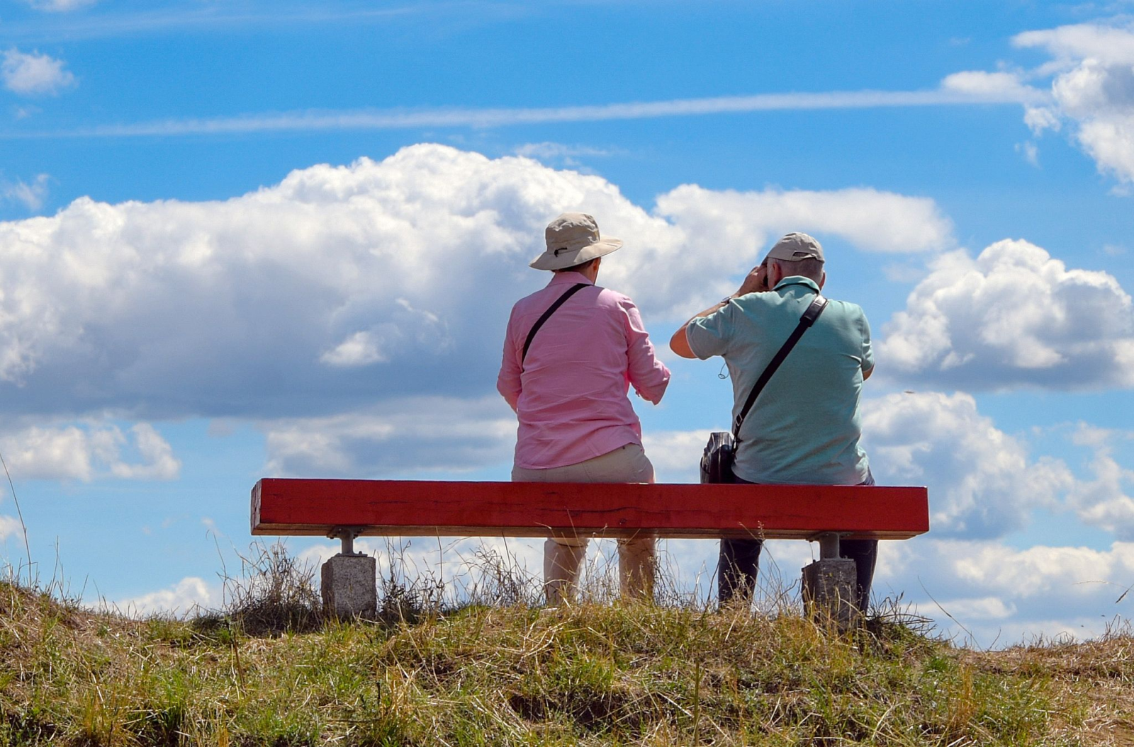 Ein Rentner und eine Rentnerin sitzen bei strahlendem Sonnenschein auf einer Bank.