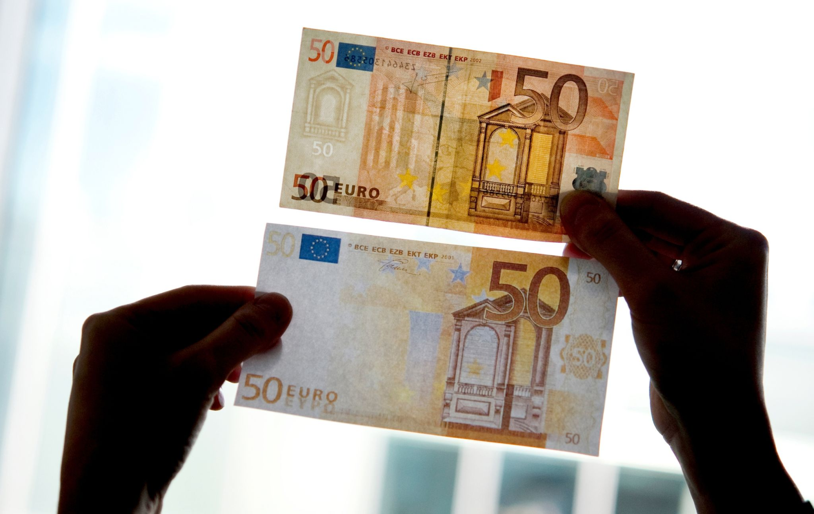 Ein echter und ein falscher Fünfzig-Euro-Schein werden gegen das Licht gehalten.