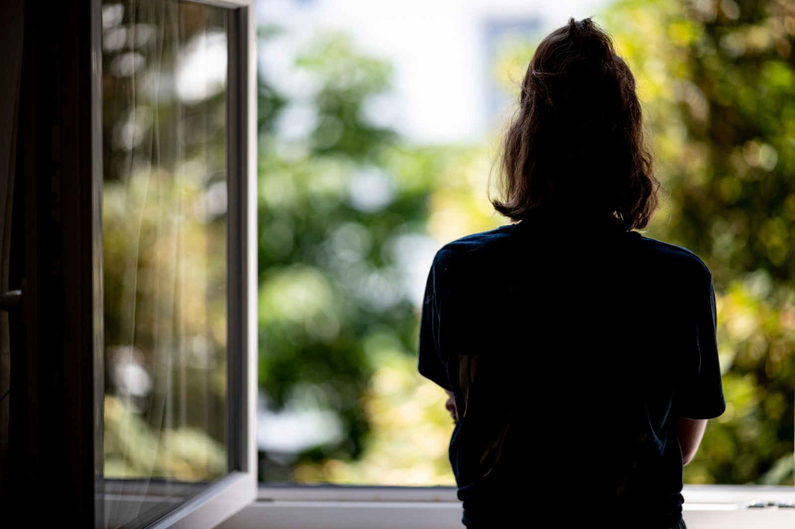 Eine Frau steht in ihrer Wohnung am Fenster.