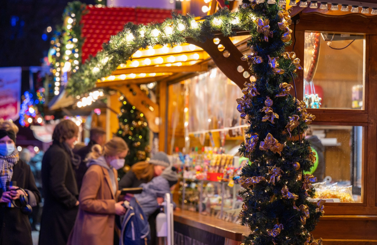Besucher eines Weihnachtsmarktes stehen an einem Verkaufsstand für Süßigkeiten.