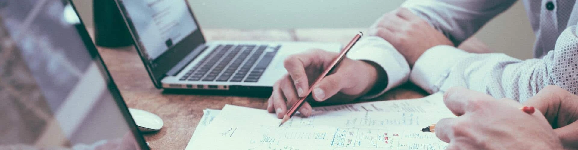 Zwei Personen sitzen am Tisch mit zwei Laptops vor ihnen. Vor ihnen liegt noch Papier, © Shutterstock Zwei Personen sitzen am Tisch mit zwei Laptops vor ihnen. Vor ihnen liegt noch Papier, © Shutterstock