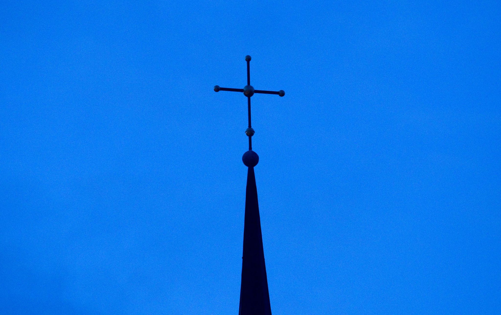 Das Kreuz einer Kirche ist in der Abenddämmerung zu sehen.