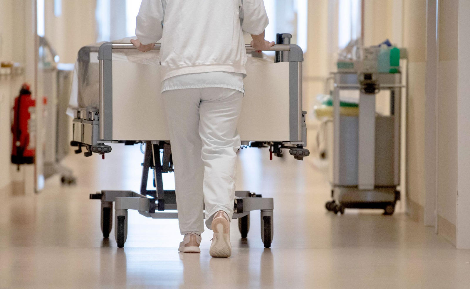 Eine Krankenpflegerin schiebt ein Krankenbett durch einen Flur., © Marijan Murat/dpa/Symbolbild