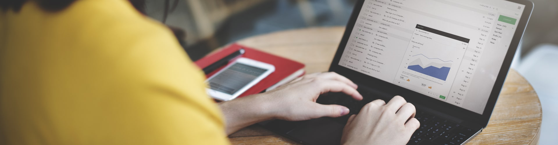Hände auf dem Laptop daneben ein rotes Notizbuch und ein Handy dadrauf, © Shutterstock