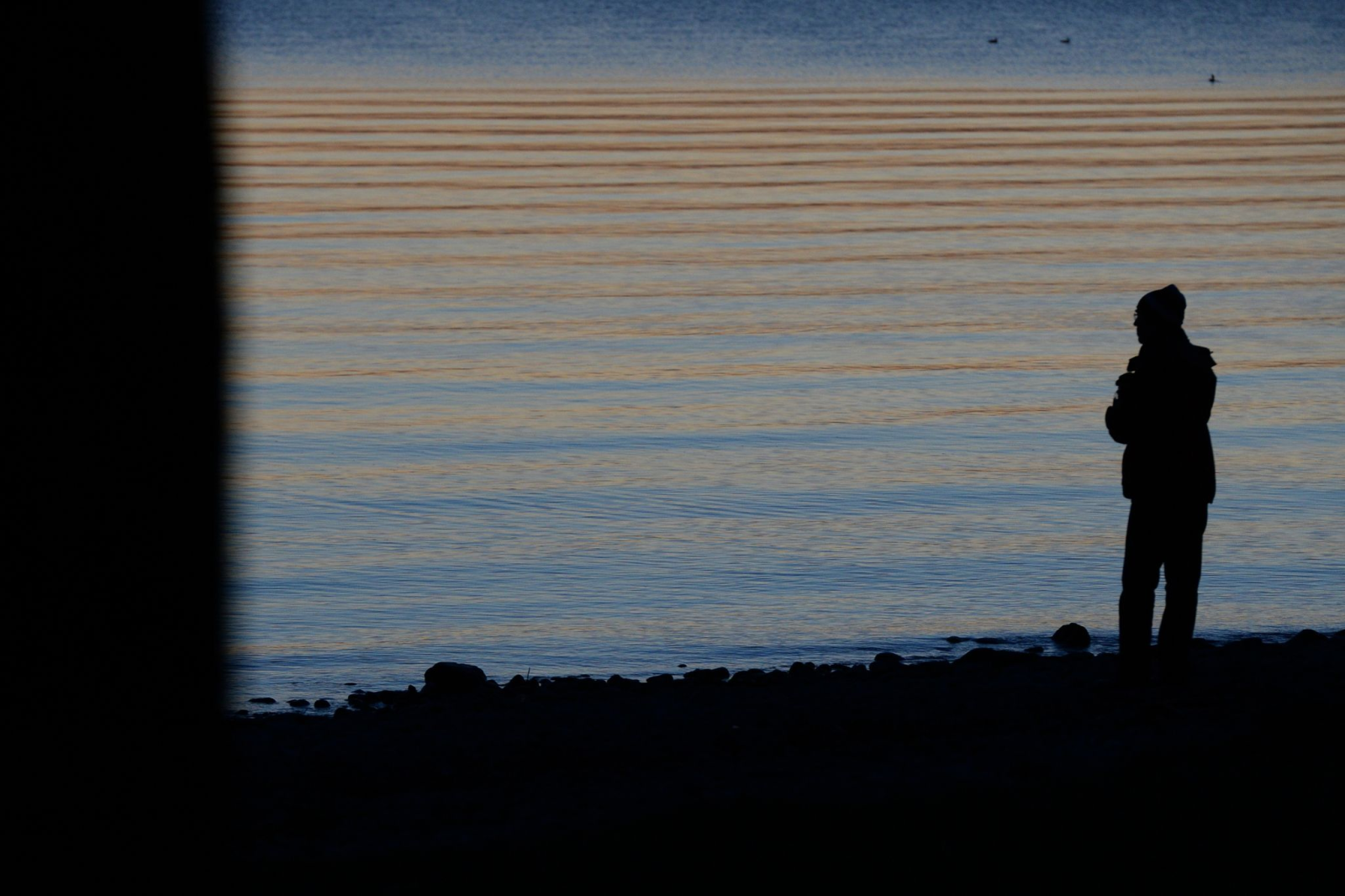 Ein Mann steht bei Sonnenuntergang am Ufer eines Sees.