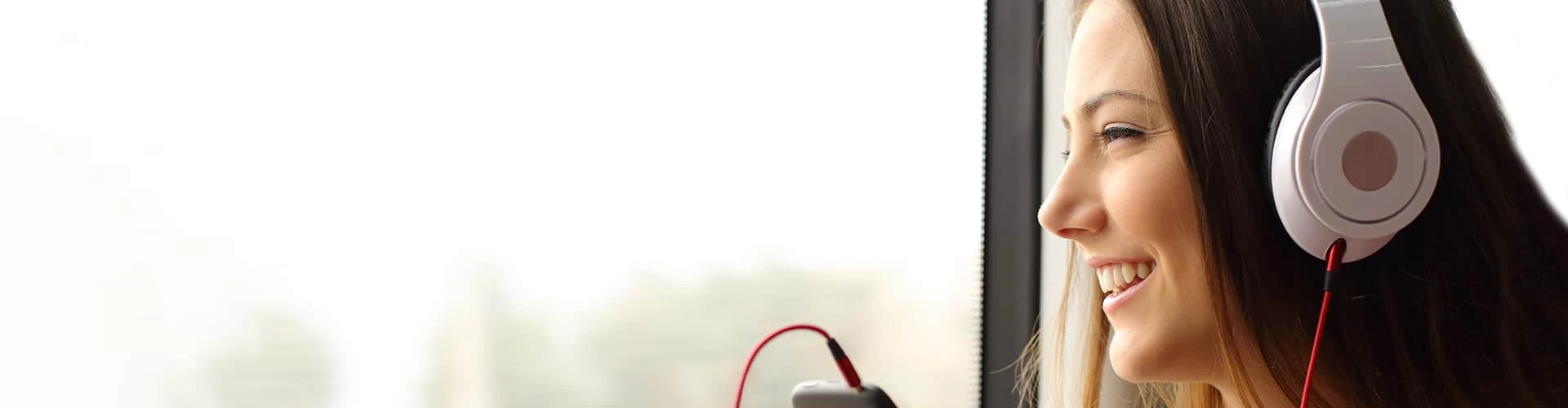 Frau mit Kopfhörern schaut aus dem Fenster und lächelt, © Shutterstock Frau mit Kopfhörern schaut aus dem Fenster und lächelt, © Shutterstock