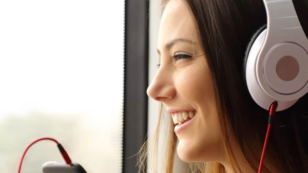 Frau mit Kopfhörern schaut aus dem Fenster und lächelt, © Shutterstock Frau mit Kopfhörern schaut aus dem Fenster und lächelt, © Shutterstock