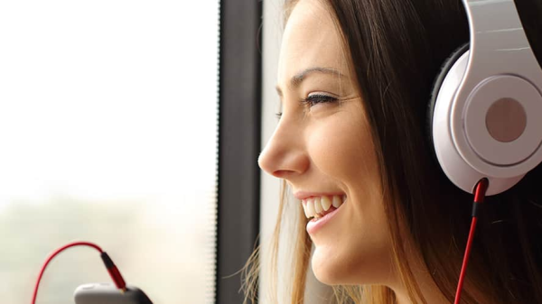 Frau mit Kopfhörern schaut aus dem Fenster und lächelt, © Shutterstock