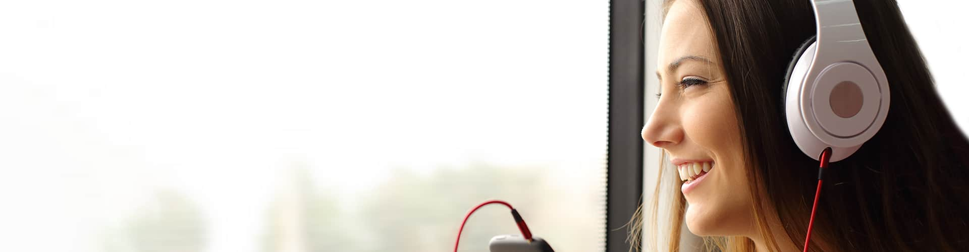 Frau mit Kopfhörern schaut aus dem Fenster und lächelt, © Shutterstock