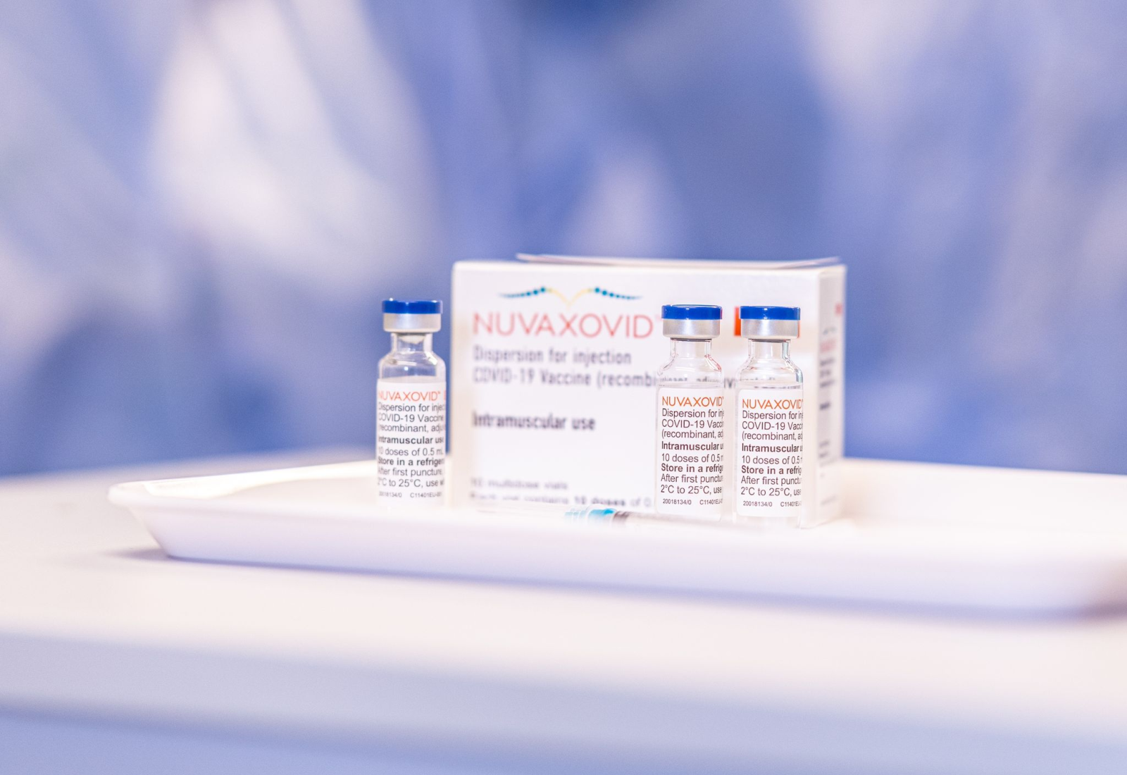 Drei Fläschchen und eine Packung mit dem Impfstoff Nuvaxovid stehen in einem Impfzentrum auf einem Tisch.