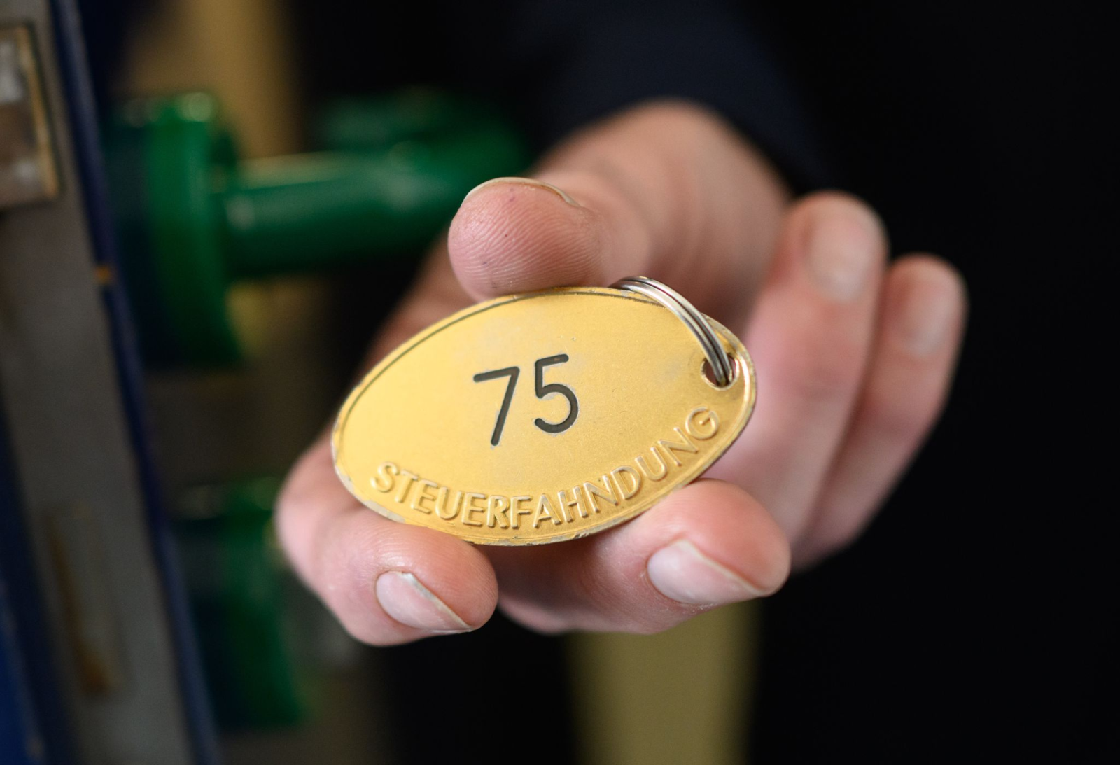 Ein Mitarbeiter zeigt im Finanzamt eine goldene Plakette mit Aufschrift «Steuerfahndung»., © Julian Stratenschulte/dpa/Symbolbild