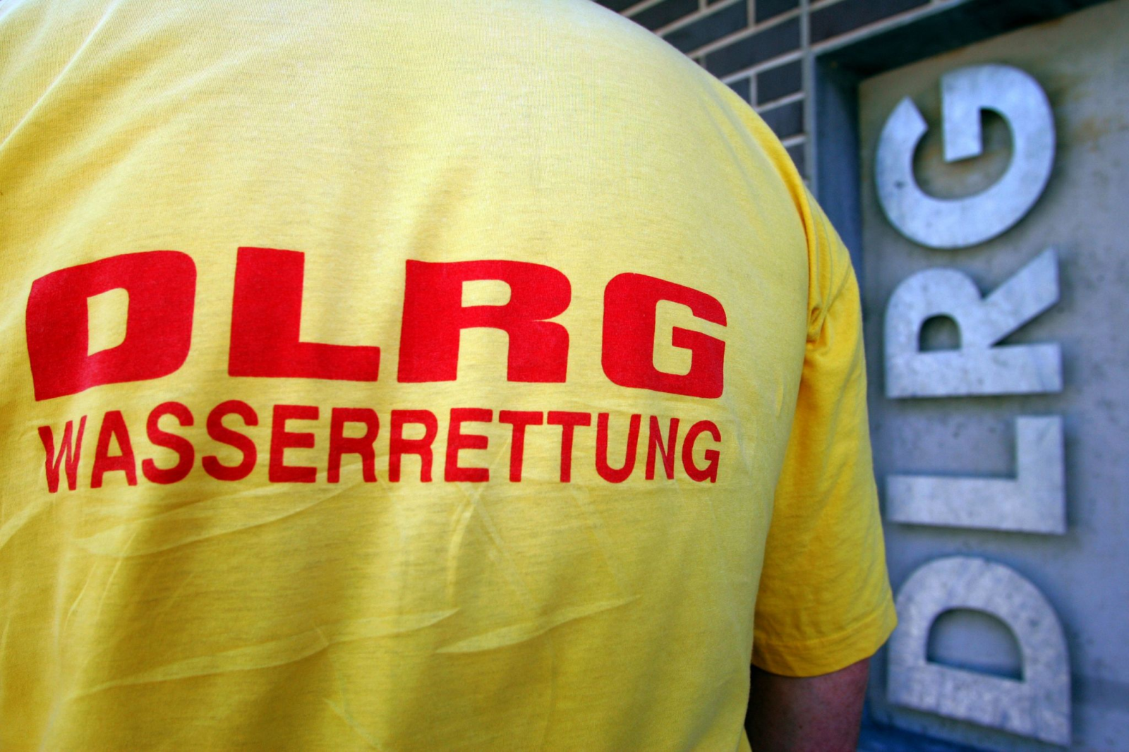 Ein Helfer der DLRG (Deutsche Lebens-Rettungs-Gesellschaft) steht vor einem Logo.