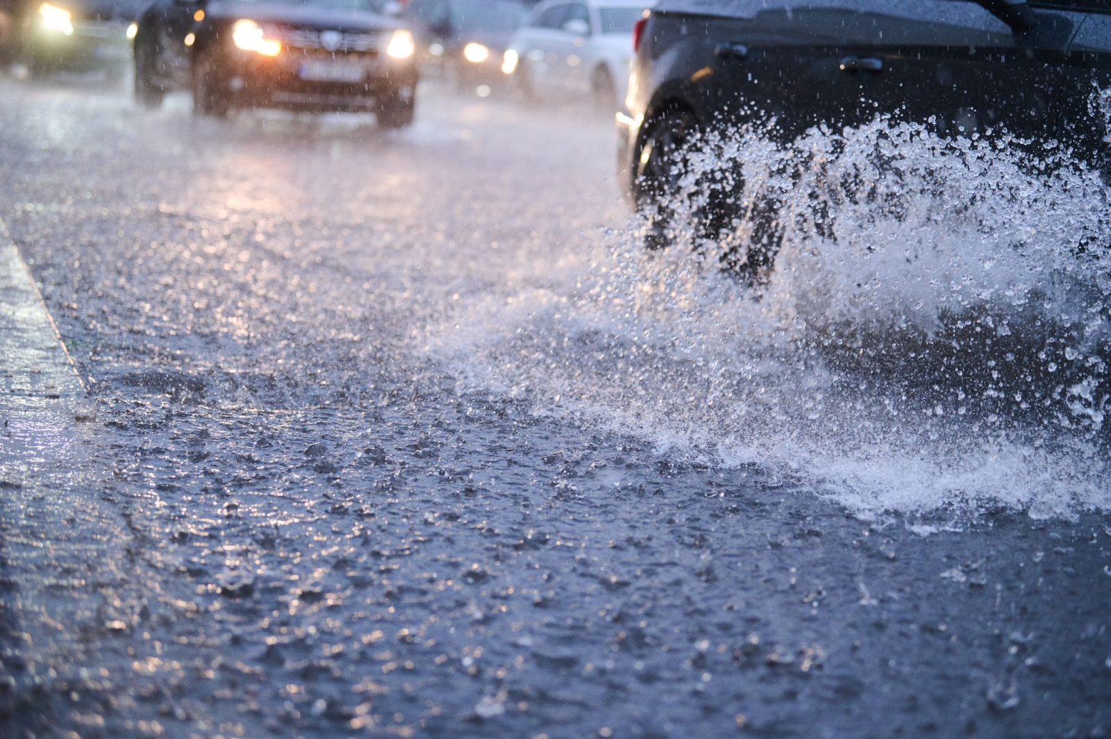 Autos fahren bei starkem Regen durch tiefe Pfützen.