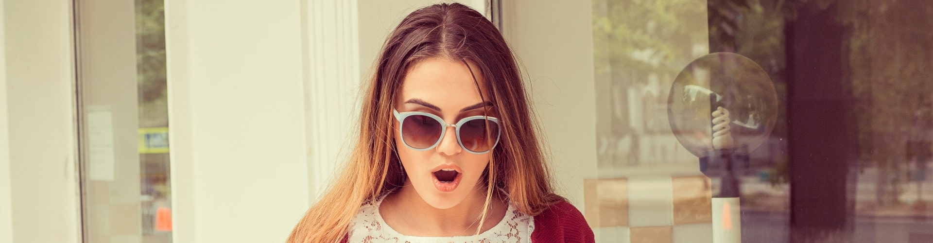 Frau mit Sonnenbrille schaut überrascht mit Mund offen runter, © Shutterstock