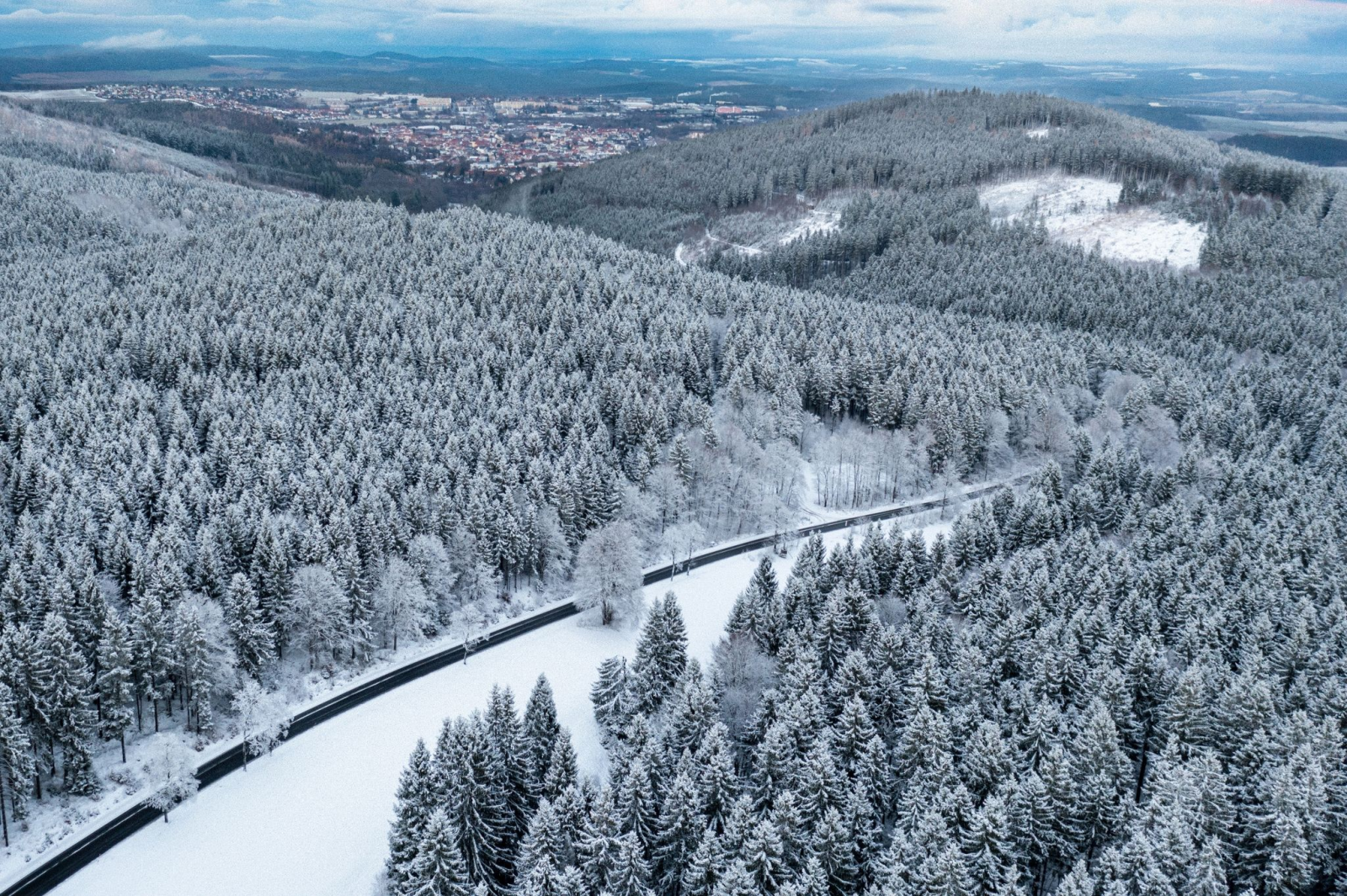 Eine Straße zieht sich wie ein schwarzes Band durch den mit Schnee bedeckten Thüringer Wald