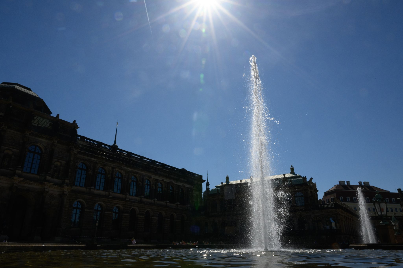 Die Sonne scheint am Himmel über einer Wasserfontäne im Dresdner Zwinger.