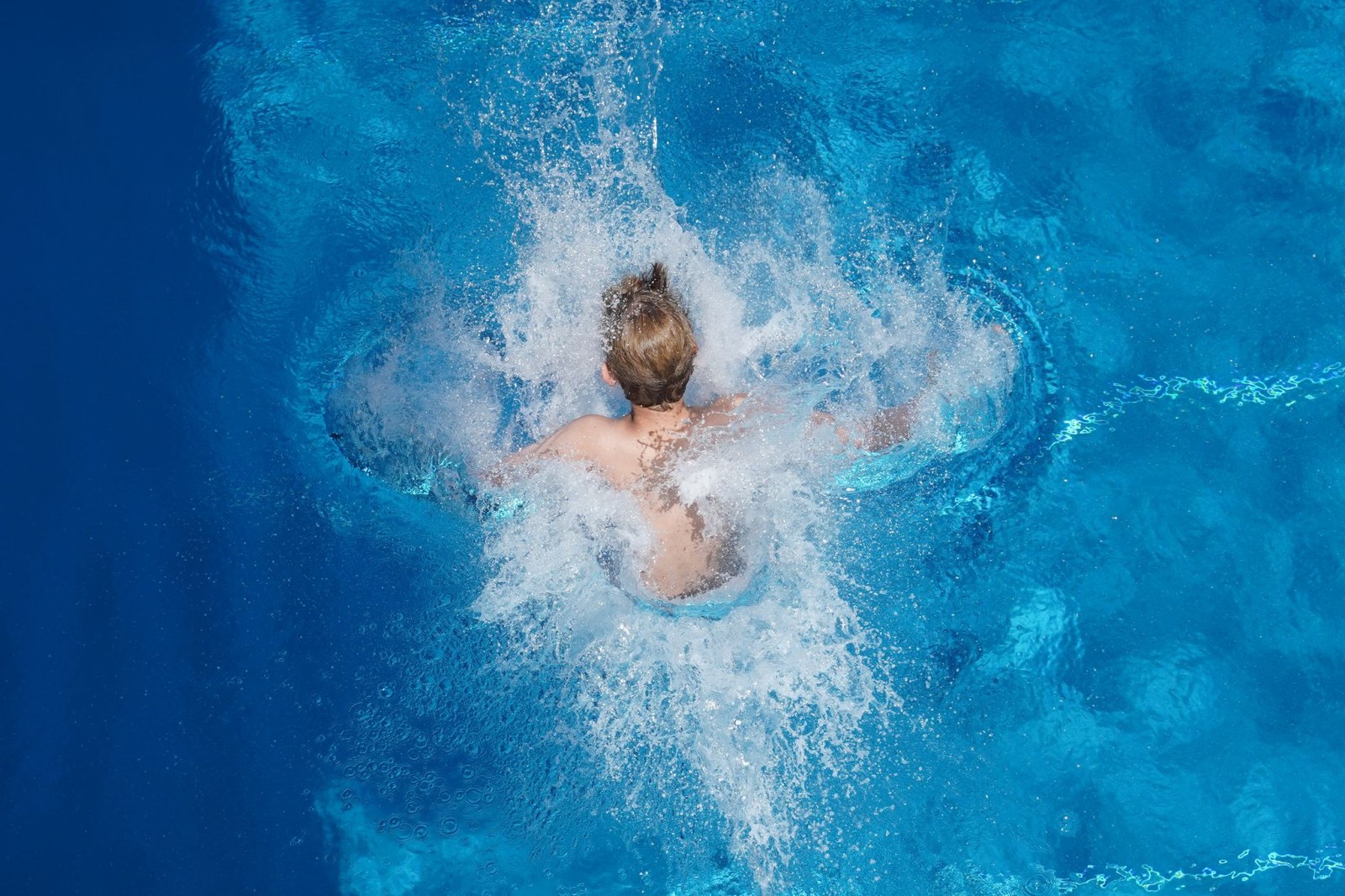 Ein Junge springt in einem Freibad ins Wasser.