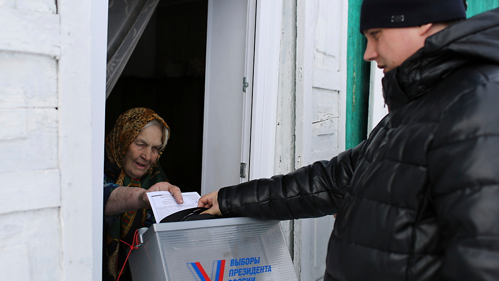 Eine ältere Frau gibt mit Hilfe eines mobilen Wahlkomitees ihre Stimme ab. Die Wähler in Russland gehen zu den Urnen, um an den Präsidentschaftswahlen teilzunehmen, bei denen es so gut wie sicher ist, dass die Präsidentschaft von Putin verlängert wird. , ©  ---/AP/dpa