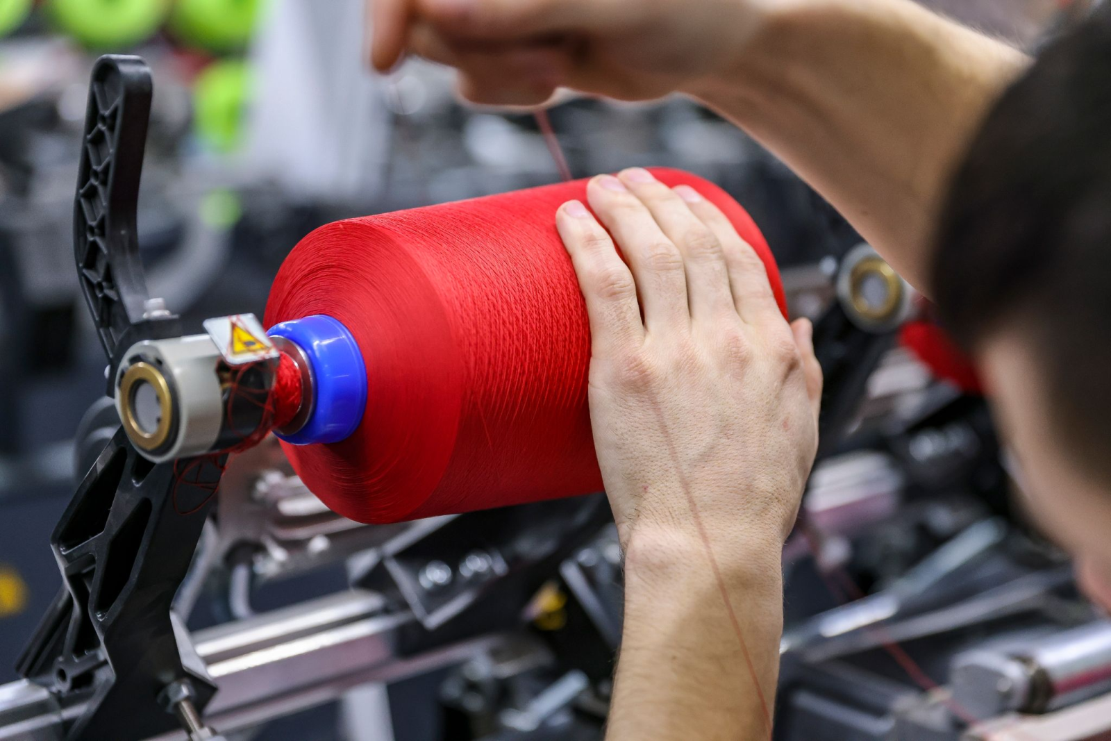 Ein Mitarbeiter wechselt in der Spulerei der OTEX Textilveredlung GmbH eine Spule mit farbigem Garn.