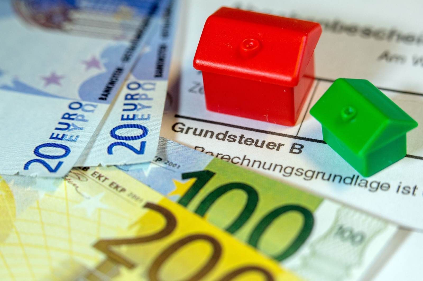 Ein Spielzeughaus und die Nachbildung von Euro-Geldscheinen liegen auf einem Abgabenbescheid für die Entrichtung der Grundsteuer.