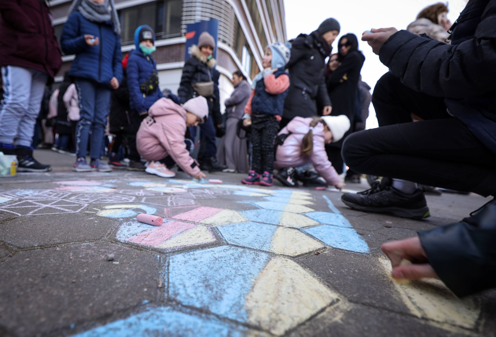 Kinder, die mit ihren Angehörigen nach deutschland geflohen sind, malen mit Kreide auf den Boden.