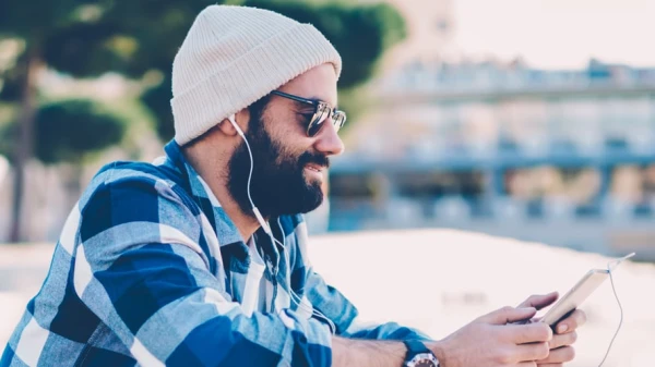 Mann im karierten Hemd hört Musik und hat eine Mütze dabei auf, © Shutterstock Mann im karierten Hemd hört Musik und hat eine Mütze dabei auf, © Shutterstock
