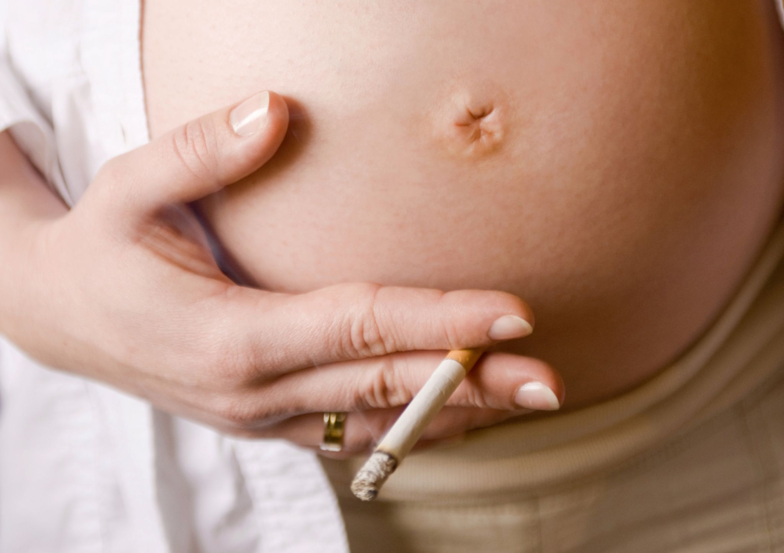 Die Hände einer schwangeren Frau mit Zigarette umfassen den Bauch mit dem künftigen Baby.