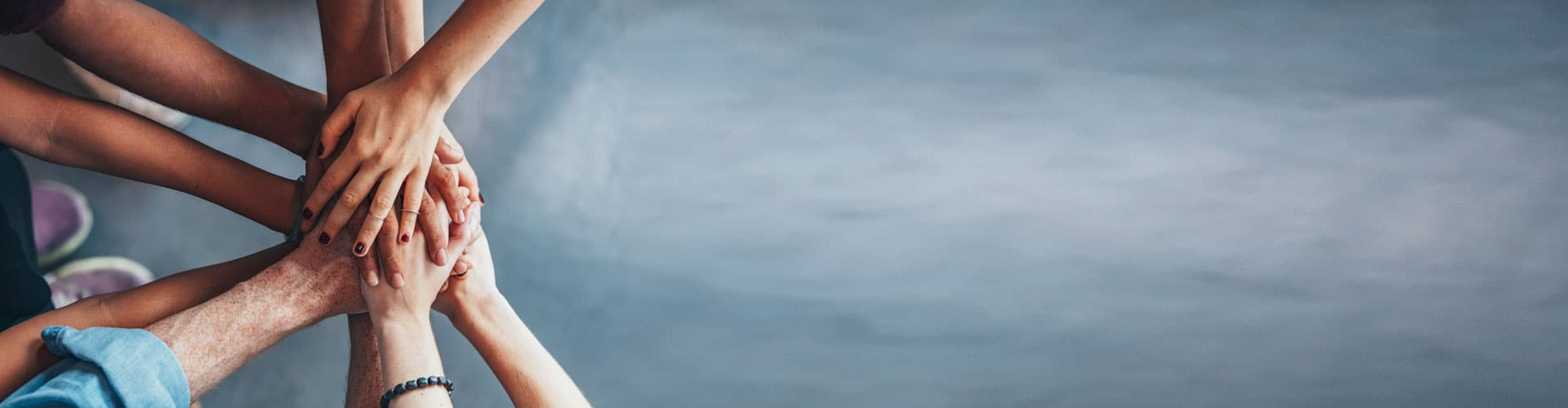 Team Bild, wie mehrere Hände aufeinander liegen. Grauer Fußboden im Hintergrund, © Shutterstock