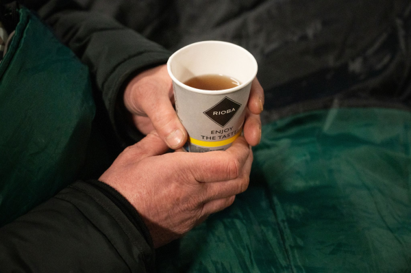 Ein Obdachloser hält einen Becher Tee in der Hand.