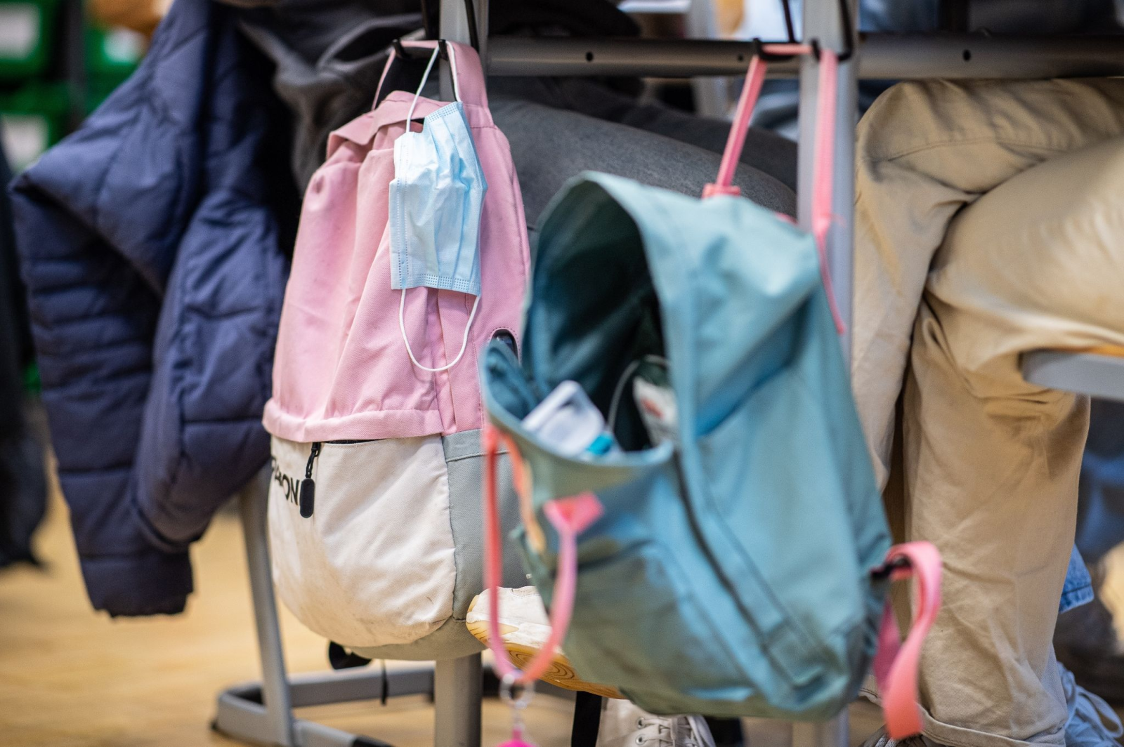 Eine Maske hängt im Klassenzimmer am Rucksack einer Schülerin.