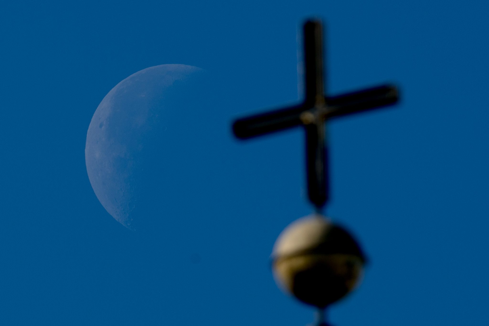 Der Mond hinter einem Kirchenkreuz.